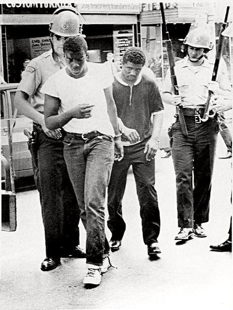 Young men handcuffed and escorted by helmeted officers
